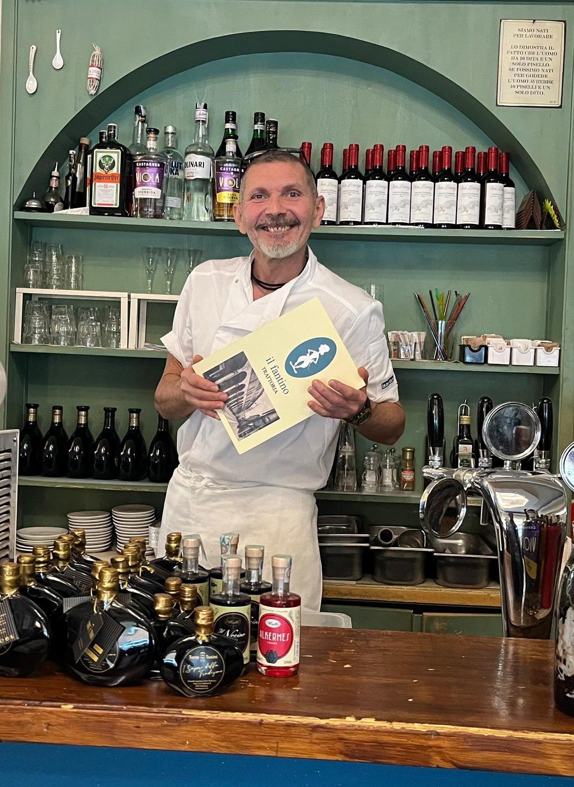 Lo chef della Trattoria il Fantino accanto allo scaffale dei vini